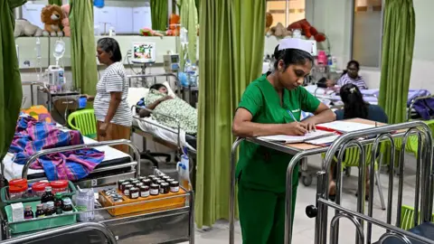 AFP via Getty Images A ward at the District General Hospital in Sri Lanka's Negombo city where dengue patients are getting treated. A nurse in green is seen taking notes in the foreground