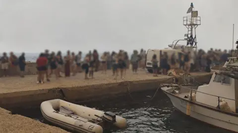 Greek fire service Blurred-out people stand on a marina pier while waiting to be evacuated in Agios Vasileios in Greece.