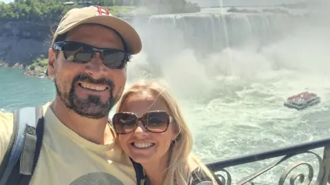 Sarah Reeve Man and woman wearing sunglasses smiling in front of a waterfall 