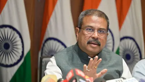 Getty Images Union Minister of Education Dharmendra Pradhan addresses a press conference at his residence, pictured with one hand up and Indian flags in the background, wearing a grey and white garment