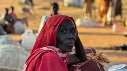 AFP via Getty Images A woman wearing a red outfit and headscarf gazes past the camera