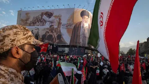 Getty Images 
An armed member of the Islamic Revolutionary Guard Corps (IRGC) monitors the area while mourners participate in the funeral for the late Supreme Leader Ayatollah Ali Khamenei and his family in Tehran, Iran, on July 6, 2026.