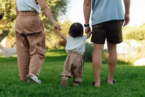 Getty Images A young toddler is led away by his parents, who are holding each of his hands