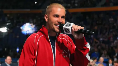Getty Images Justin Bieber wears a read jacket and holds microphone with an NHL logo on it while he attends the 2026 NHL Draft on 26 June 2026 in Buffalo, New York
