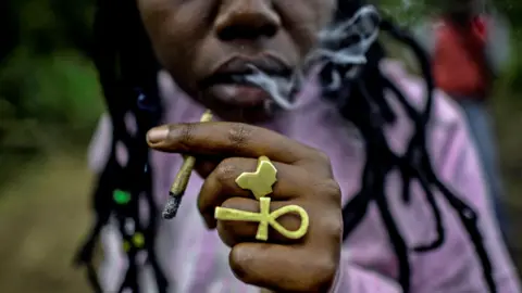 AFP via Getty Images A Rastafarian men holde a cigarette from which smoke is rising.