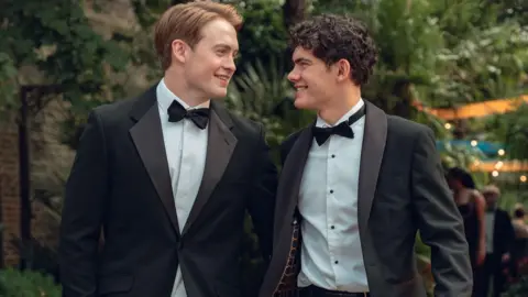 Netflix Production still from Heartstopper Forever showing Kit Connor and Joe Locke smiling at each other in tuxedos