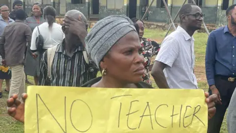 John Alabi /  BBC A woman holds up a banner at a protest at a school.