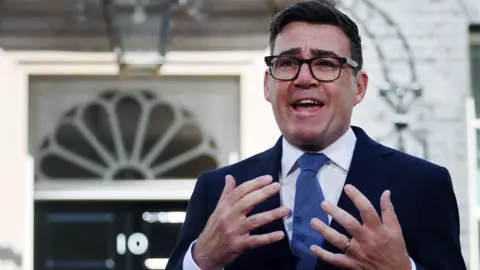 EPA/Shutterstock Andy Burnham, dressed in a navy suit, white shirt and ties, stands in front of No 10 Downing Street making a speech