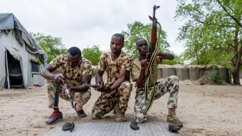 AFP via Getty Images Three Nigerian soldiers wearing army fatigues appear to load their guns
