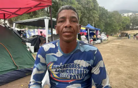 Victor Calderón wearing a blue T-shirt, sits among a row of tents on a golf course which is now his home after the building he lived in collapsed.