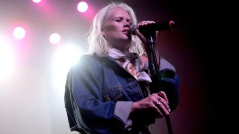 Getty Images Lauren Bennett sings onstage during a concert. She wears a denim jacket