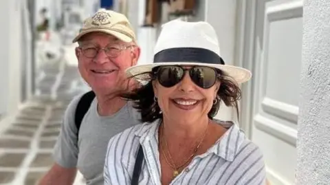 Alan Carter Karen Carter, pictured with her husband Alan. She is wearing dark glasses, a black and white sun hat and a white and striped shirt. 