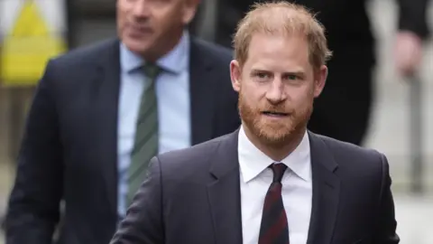 PA Media Prince Harry wearing a dark suit with a maroon tie.