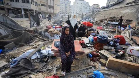 Reuters A Palestinian woman sits amidst debris as people inspect the site of an Israeli strike on a house in Gaza City, 30 July 2026.