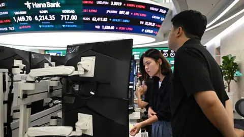 AFP via Getty Images Currency dealers watch monitors as an electronic screen shows South Korea's benchmark stock index (KOSPI) in a foreign exchange dealing room at the Hana Bank headquarters in Seoul on July 28.