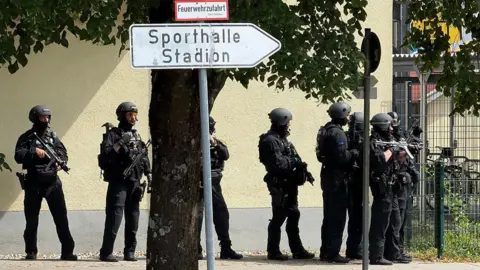 AFP via Getty Images Police officers stand with guns outside a school in Germany.