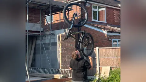 BBC Man with a bicycle balanced on his chin.