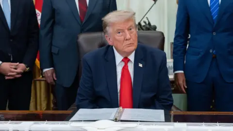 EPA US President Donald Trump sitting in the White House wearing a blue suit jacket, white shirt and red tie. 