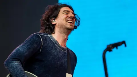 Getty Images Gary Lightbody of Snow Patrol smiles as he performs on stage at the Latitude Festival in 2025, against a light blue backdrop