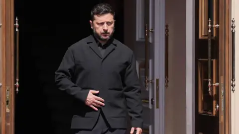 PA Media Zelensky, wearing a dark suit, walking through a doorway