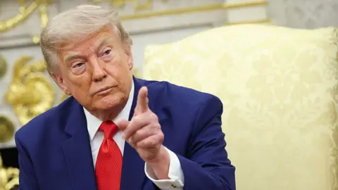 Getty Images President Donald Trump pointing his finger. He has a serious look on his face and is wearing a blue suit with a white shirt and red tie.