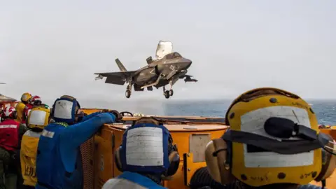US Central Command / X US service members aboard the USS Boxer amphibious assault ship watch a US fighter jet in flight. File photo