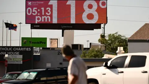 Getty Images Man walks through road and looks up at sign that says 118 degrees and 05:15 pm