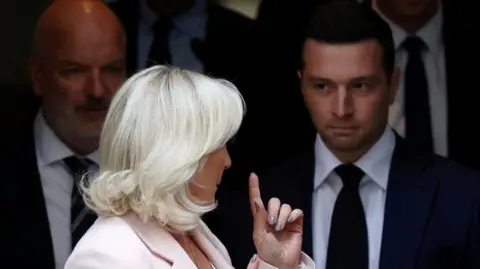 EPA Le Pen raises a finger while looking back at a man with a dark suit and tie and a white shirt