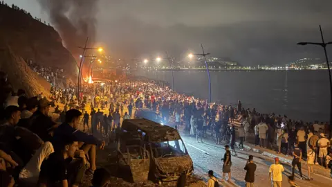 Reuters Crowds gather around a torched vehicle while waiting for a chance to cross to the Spanish enclave of Ceuta, on the Moroccan side of the border in Fnideq, Morocco