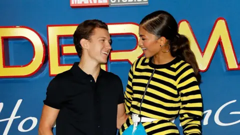 Getty Images Tom Holland and Zendaya at the premiere for Spider-Man: Homecoming in 2017. Holland is wearing a black polo shirt and Zendaya is wearing a yellow and black striped top.