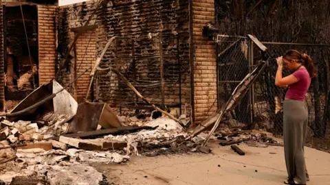 Reuters A woman holds her hand to her head as she looks at the rubble of a house. The bricks of the building are charred