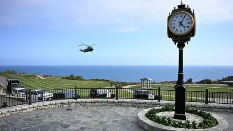 Getty Images Trump's White House helicopter seen landing at the California golf course on Tuesday. There is a clocktower in the foreground and golf greens and ocean in the background