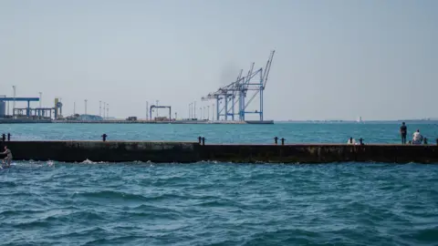 Getty Images A man on a pier looks at a line of cranes in the distance at Odesa's port. There is not a single ship in the shot, showing how empty the docks are amid recent Russian attacks