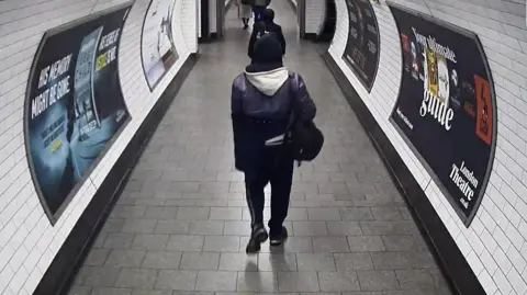 PA CCTV image of a London Underground passageway showing several people walking through a tiled corridor, including Levy.
