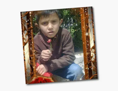 A photo of seven-year-old Wael, wearing a brown jumper and blue jeans, and holding a red flower 