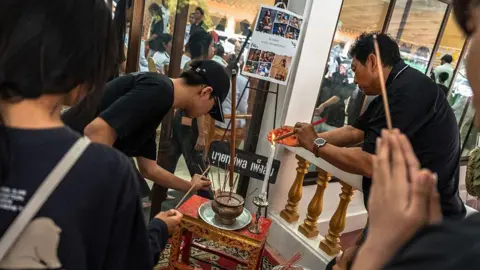 AFP via Getty Images People wearing black pray with joss sticks in front of a small table