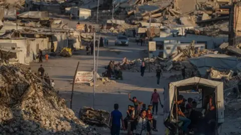 EPA/Shutterstock A wide view of displaced Palestinians walking between destroyed houses in Jabaliya, northern Gaza City, on 7 August.