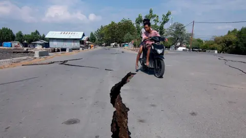 EPA/Shutterstock A motorcyclist rides past a crack on the road following the earthquake in East Nusa Tenggara Province, Indonesia.