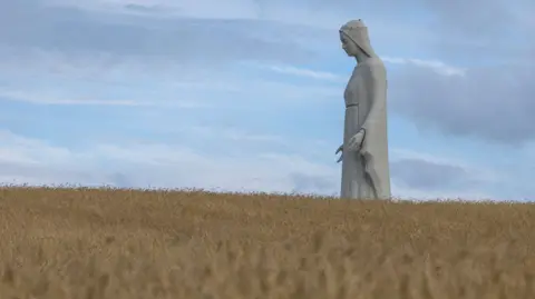 Getty Images A statue of the Virgin Mary rises above a wheat field.