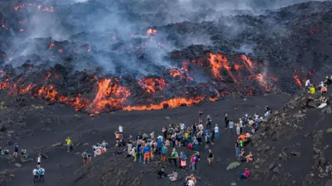 EPA People gather to watch as lava flows down Mount Etna during a period of heightened volcanic activity, near Catania, Sicily, southern Italy, 13 August 2026. 