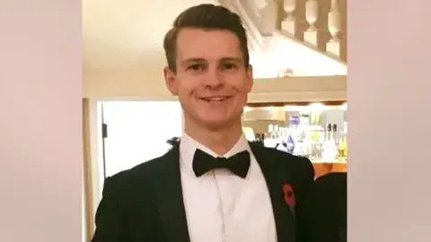 Social Media  Alexander Cromie smiles in a tuxedo while holding a glass of wine.