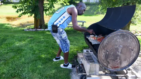 Reuters A man in a blue sports vest and jean shorts grills food in a garden