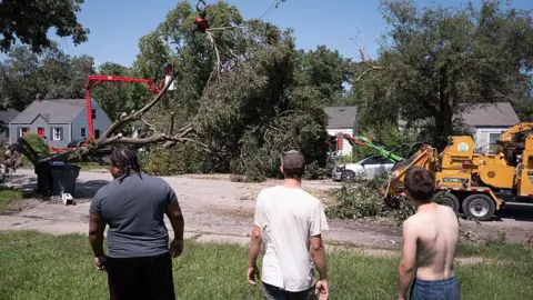 Getty Images Three men watch as large tree that has fallen is cut