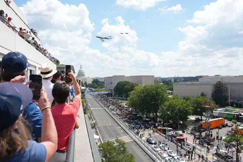 Getty Images People take photos on a rooftop as Air Force one takes part in a flyover with the Capitol building in the background and the racetrack below
