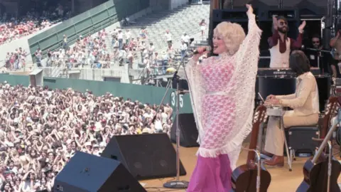 Richard McCaffrey/Michael Ochs Archive A side view of Parton singing on stage, and you can see the huge crowd watching her.