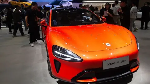 NurPhoto via Getty Images A bright orange Xiaomi SU7 sedan displayed at a Xiaomi booth at the National Exhibition Center in Shanghai, China in April 2025.
