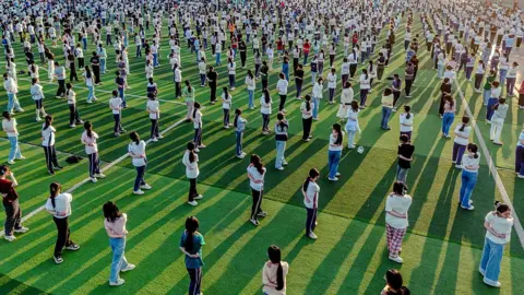 Getty Images Hundreds of students practise yoga on a sports pitch to relieve stress before the annual China's National College Entrance Exam. They are spaced equally apart and are wearing normal clothes, not school uniform.
