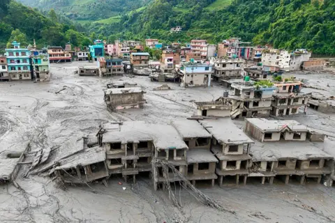 AFP via Getty Images An aerial view shows houses lying deluged in sludge after flash floods at Devighat, Bidur Municipality in Nepal's Nuwakot district on August 27, 2026. Nepal's disaster agency said that 823 people remained out of contact on August 27, more than 24 hours after a deadly flood tore through the border region with Tibet. (Photo by Prabin RANABHAT / AFP via Getty Images)