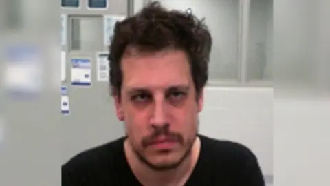 DHS DHS released an mugshot of Yiannopoulos after his arrest. He wears a black shirt and has facial hair