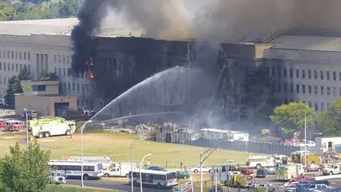 Getty Images Smoke comes out from the west wing of the Pentagon on 11 September 2001 while fire engines spray water into the buildings.